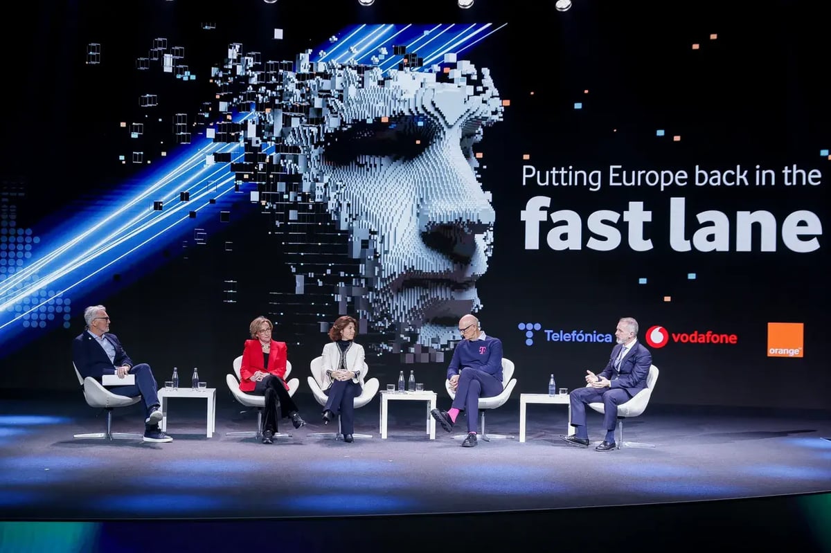 A panel discussion at MWC25 features five executives seated on a stage with a futuristic digital backdrop displaying the phrase 'Putting Europe back in the fast lane' along with logos of Telefónica, Vodafone, and Orange. The stage is illuminated with blue lighting and a digital face graphic made of pixelated blocks. The panelists, dressed in professional attire, are engaged in conversation, with one speaker gesturing while others listen attentively.